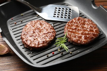 Pan with grilled patties, spices and slotted spatula on wooden table, closeup