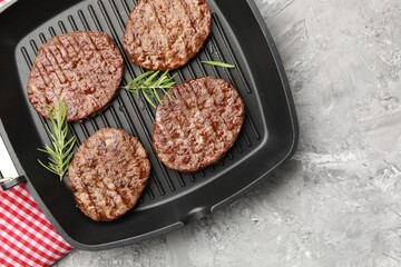 Pan with grilled patties and rosemary on grey table, top view. Space for text