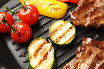 Grilled beef steaks and vegetables on black pan, above view