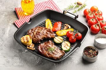 Pan with grilled beef steaks, mushrooms, vegetables and spices on grey textured table, closeup