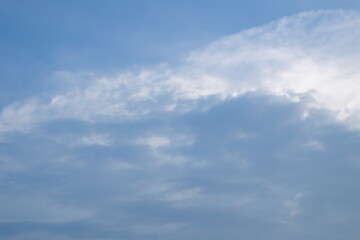 A view of a partly cloudy sky with sunbeams piercing through. Dark clouds sit at the bottom left, contrasting with the brighter, scattered clouds and the clear blue sky. High quality photo
