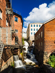 Summer view of a serene waterfall flowing through old industrial buildings in Sweden