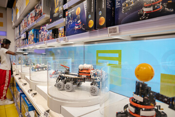Naklejka premium New York City, New York, USA - 07.31.2024: A LEGO space exploration rover is exhibited inside a transparent case on a toy store shelf. The background features multiple boxed LEGO Technic space sets