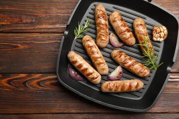 Pan with grilled sausages and spices on wooden table, top view. Space for text
