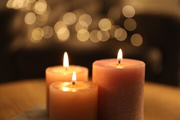 Burning candles on table against blurred lights indoors, closeup