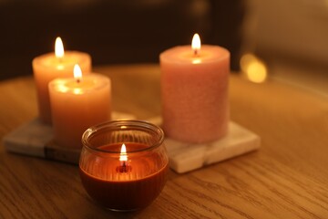 Burning candles on wooden table indoors, closeup