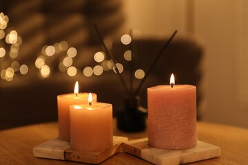 Burning candles and reed air freshener on wooden table against blurred lights indoors, closeup
