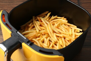 Air fryer container with cooked french fries on wooden table, closeup