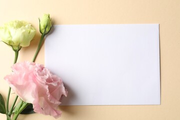 Blank card and flowers on beige background, flat lay