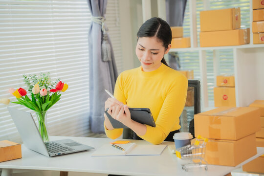 Cheerful Asian small business owner working in office with online sales and package delivery in home office.