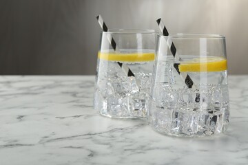 Refreshing water with lemon and ice on white marble table, closeup. Space for text