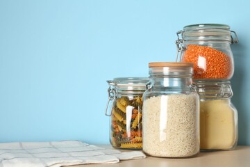 Glass jars with different products on wooden table against light blue background. Space for text
