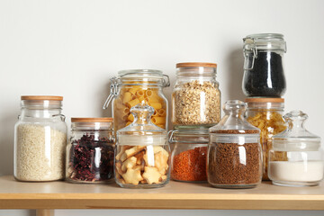 Glass jars with different products on wooden table near white wall