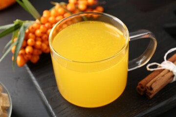 Sea buckthorn tea in glass cup, fresh berries and cinnamon on black table, closeup