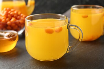 Sea buckthorn tea in glass cups, honey and fresh berries on black table, closeup