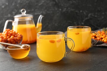 Sea buckthorn tea in glass cups, teapot, honey and fresh berries on black table, closeup