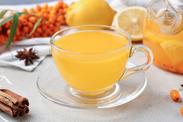 Sea buckthorn tea in glass cup, teapot, spices, lemon and fresh berries on light grey table, closeup