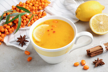 Sea buckthorn tea in cup, spices, lemon and fresh berries on light grey table, closeup