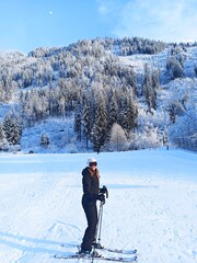 Athlete skiing on the slope on vacation in the mountains. Fashion ski vacation. Fashion girl skiing in the Alps. Model posing with frozen forest background. Landscape of ski slopes. Ski resort. Blog.
