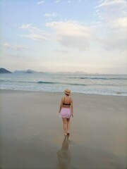 Woman with her back turned dressed in a short skirt walking alone on the beach.Copacabana beach Praia de Copacabana Rio de Janeiro. Brazil. Young girl walking on a beach at sunset in a romantic scene 