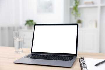 Fototapeta premium Modern laptop with blank screen and notebook on wooden table indoors. Mockup for design