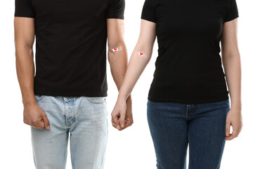 Blood donation. Man and woman with adhesive bandages holding hands on white background, closeup