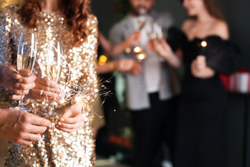 Friends celebrating New Year with sparklers and wine glasses indoors, closeup
