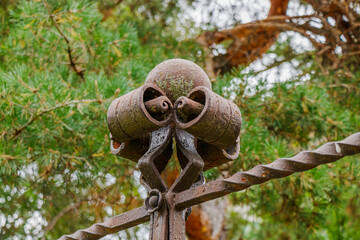 Close-up of ornate wrought iron finial with curled metal details on a gate against a background of pine trees