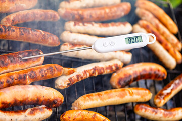 Grilled sausages on barbecue with thermometer confirming meat readiness temperature