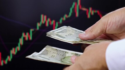 Close up view of man hands, Indian rupee banknotes, market chart on computer screen in background. Concept of currency growth, stock price change, volatile financial market, internet trading in India. - Powered by Adobe