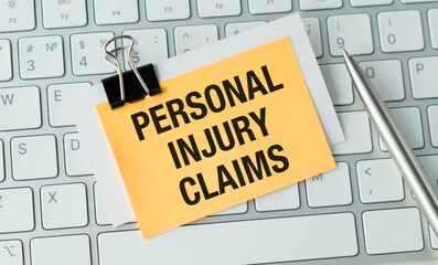 Personal Injury Claims Text on a yellow sticky note with a clip on a keyboard with a pen