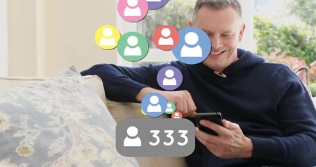 Mature man tapping smartphone on couch monitoring social media count with icons rising to 763 - Powered by Adobe