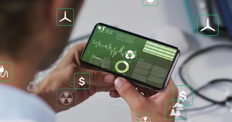 Man raising smartphone at desk while monitoring green energy data and showing floating energy icons - Powered by Adobe