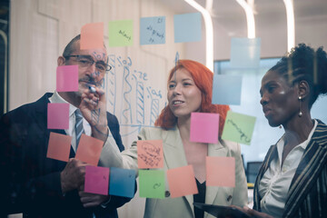 Diverse business team brainstorming ideas using sticky notes and digital tablet in modern office, teamwork and collaboration in creative planning session.