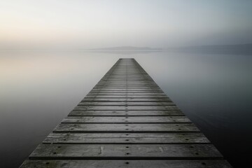 Weathered wooden pier extending into calm misty lake at dawn water