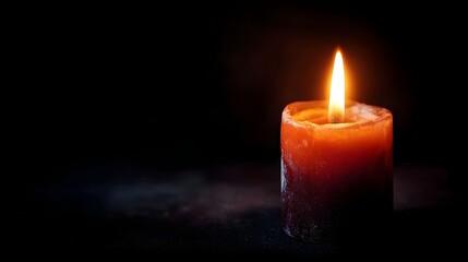 Fototapeta premium A single candle flame burns brightly in the darkness casting a warm atmospheric glow