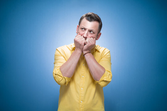 Fototapeta Worried young man biting her fingernail, she know the secret over blue background, dresses in yellow shirt