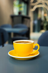 A cup of black coffee americano in a yellow cup in a cafe with copy space
