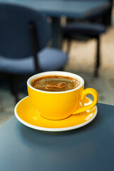 A cup of black coffee americano in a yellow cup in a cafe with copy space
