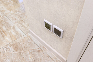 Interior shot featuring two digital thermostats mounted on a textured wall. Marble floor tiles add...