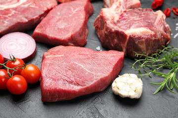 Pieces of raw beef meat, spices and tomatoes on black table, closeup