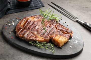 Delicious grilled beef steak with herbs, spices and carving fork on grey textured table, closeup