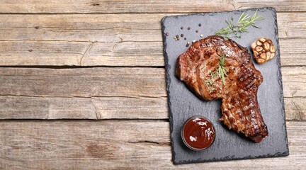 Delicious grilled beef steak with herbs, spices and ketchup on wooden table, flat lay. Space for text