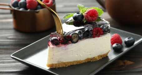 Eating piece of delicious cheesecake with berries and mint at wooden table, closeup