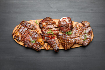 Pieces of tasty grilled beef with rosemary on black wooden table, top view