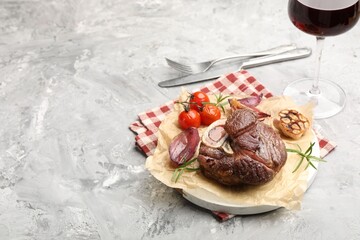Tasty cut beef steak served with rosemary, garlic, tomatoes and wine on grey textured table, space for text