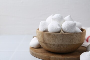 Delicious meringue cookies in bowl on white tiled table, closeup. Space for text
