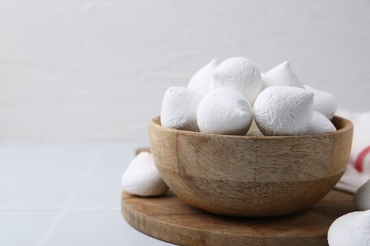 Delicious meringue cookies in bowl on white tiled table, closeup. Space for text