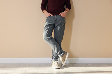 Man in stylish jeans near beige wall indoors, closeup