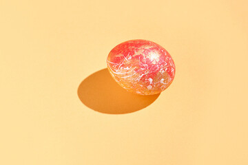 Vibrant red speckled easter egg on soft pastel orange background with shadow.